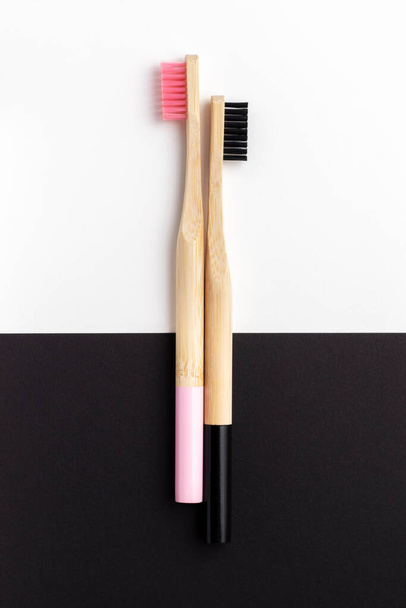 Dos cepillos de dientes de madera con cerdas negras y rosadas sobre fondo blanco y negro. Vista superior. - Foto, imagen