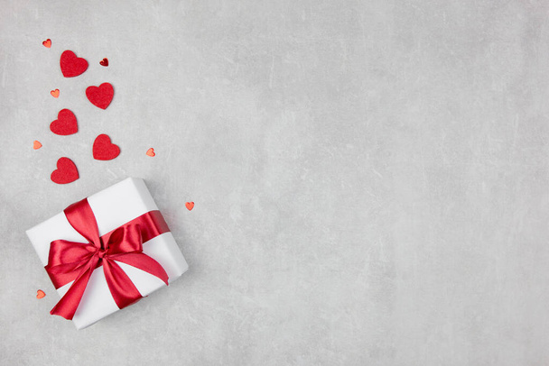 Valentijnsdag achtergrond met geschenk en rode harten confetti op lichte betonnen achtergrond. Valentijnsdag of moederdag, verjaardag, vakantie concept. Vlakke lay, bovenaanzicht, kopieerruimte. - Foto, afbeelding