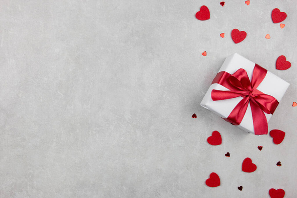 Valentines Day background with gift and red hearts confetti on light concrete background. Valentines or mothers day, birthday, holiday concept. Flat lay, top view, copy space. - Fotografie, Obrázek