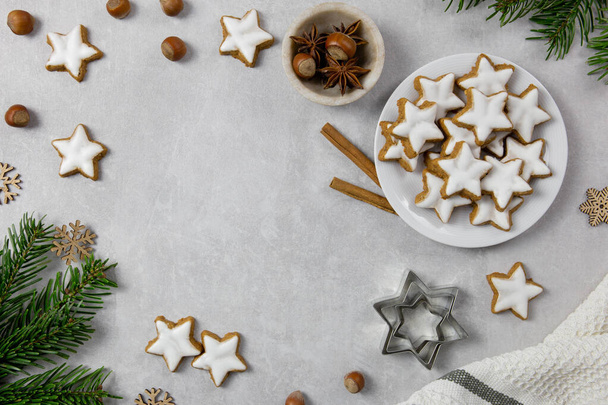 Christmas traditional German cookies, cinnamon stars with hazelnuts, decoration and tree branches on a light concrete background. Top view. Copy space. - Foto, imagen