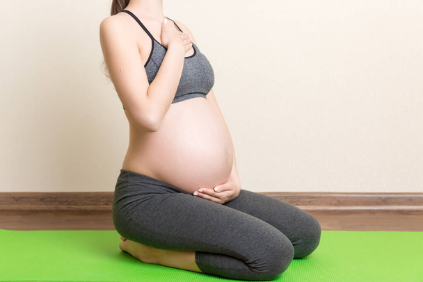 Odada yeşil paspas üzerinde egzersiz yapan hamile bir kadın. Coronavirus zamanında hamilelik Yogası ve Spor Konsepti. - Fotoğraf, Görsel