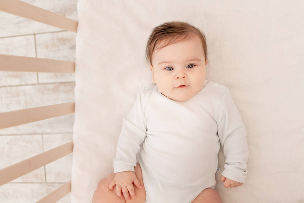 aranyos baba hat hónappal ezelőtt feküdt egy bölcsőben egy fehér kosztümben - Fotó, kép