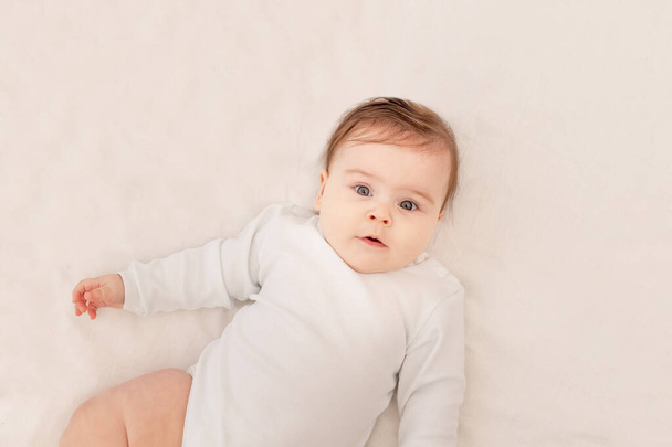 かわいい赤ちゃん6ヶ月白いボディスーツのベビーベッドに寝そべって - 写真・画像