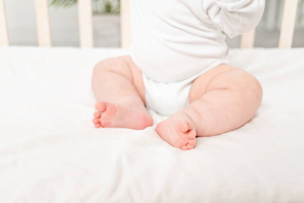 legs of a small child sitting in a crib - Foto, Bild