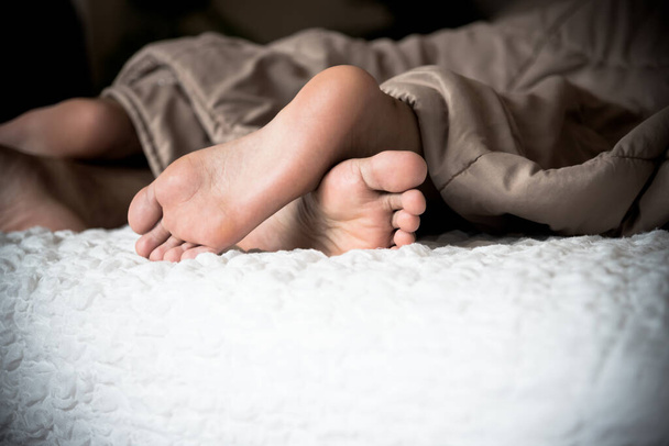 恋人の足は毛布から出てきた彼らは両方の白いベッドの上に横たわっていたカップルやバレンタインデーのコンセプトに. - 写真・画像