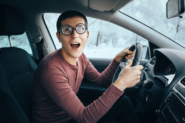Divertido y ridículo conductor nerd idiota en gafas grandes sosteniendo el volante y sonriendo a la cámara. Concepto de conductor novato distraído de la carretera - Foto, Imagen