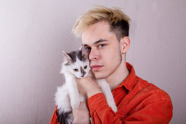 灰色の背景に猫を抱いている10代の若者の肖像画。コンセプト:ペット、動物の世話、弟への愛. - 写真・画像