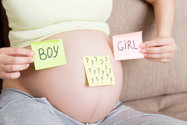 pregnant woman holding square multicolored stickers with question marks. - Photo, image