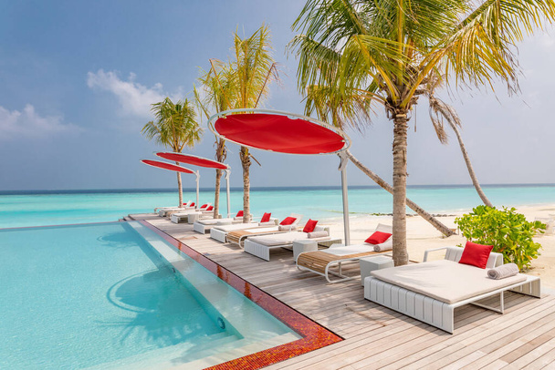 Tourismuslandschaft im Freien. Luxuriöses Strandresort mit Pool und Liegestühlen oder Liegestühlen unter Sonnenschirmen mit Palmen und blauem Himmel. Sommerreise und Urlaubshintergrundkonzept - Foto, Bild