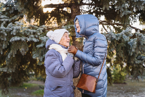 Motherhood. Theme importance visiting and spending time with old single parents during holidays. Senior mom and mature daughter happy family hug and laugh in park background Christmas tree in winter. - Photo, Image