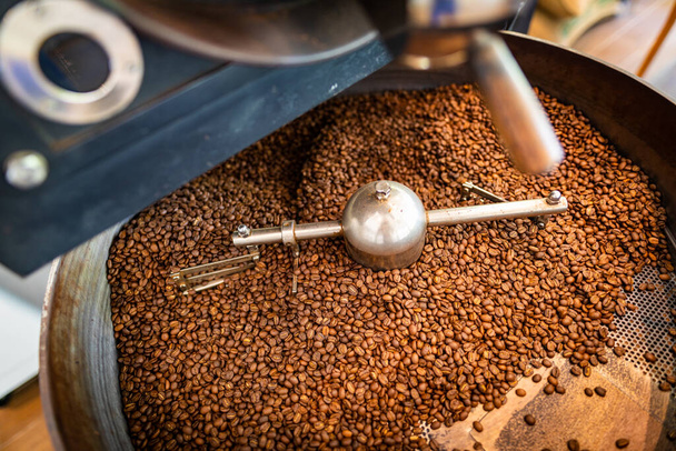 grains de café aromatiques fraîchement torréfiés dans une machine de torréfaction de café moderne. mélange de café torréfié, grains de café sont mélangés dans le cylindre de refroidissement - Photo, image