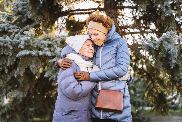 Femmes caucasiennes mère aînée et fille mature dans le jardin d'hiver sur fond sapin étreindre les uns les autres face à face, sourire, passer du temps avec de vieux parents, marcher avec maman âgée dans la forêt pour Noël - Photo, image