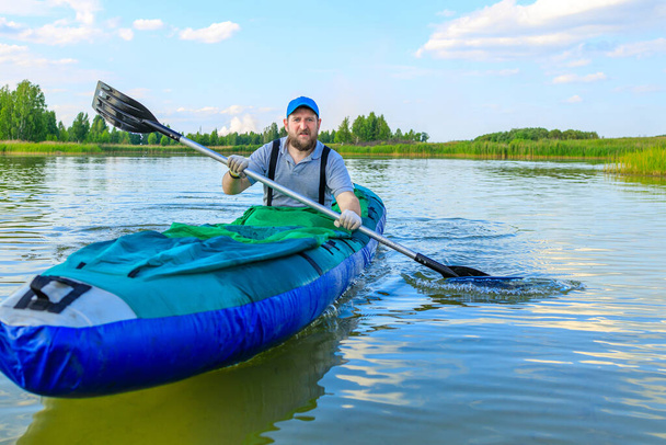hombre barbudo en una camiseta gris remando remos en un kayak inflable, caminando sobre el agua en el verano. naturaleza viaja a través de aguas nativas - Foto, Imagen