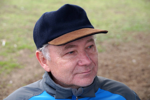 портрет улыбающегося мужчины средних лет в кепке на естественном фоне - Фото, изображение