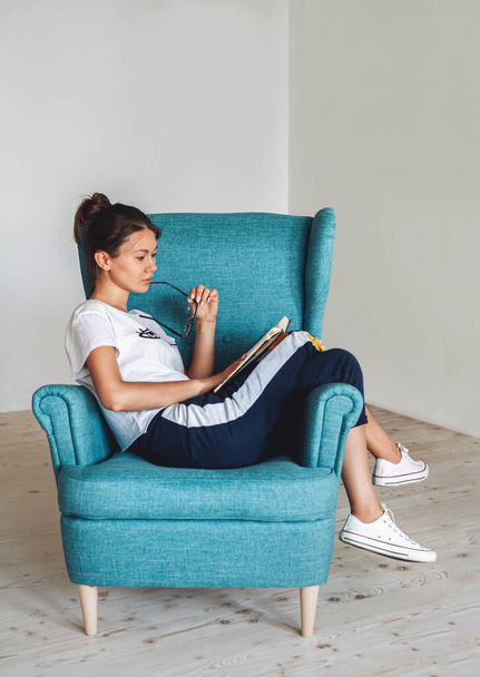 Young woman sitting in the armchair and reading book, isolated - Foto, Imagem