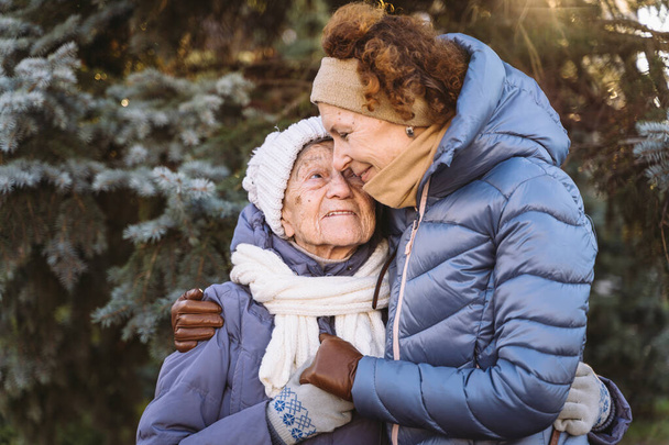 Paar blanke volwassen vrouwen en oudere vrouwen zijn blij om samen tijd door te brengen op kerst- en nieuwjaarsvakantie, glimlachend en knuffelend in het bos op de achtergrond van dennenboom bij zonnig weer. - Foto, afbeelding