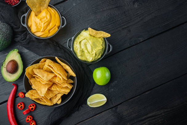 Fichas de nachos mexicanos con salsas de queso y guacamole, sobre fondo de madera negra, vista superior o plano con espacio de copia para texto - Foto, imagen