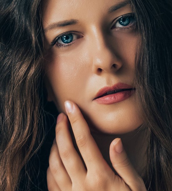 Beautiful woman applying cosmetics with her hand on face, natural look and wavy long hairstyle, beauty portrait and skincare routine - Fotoğraf, Görsel