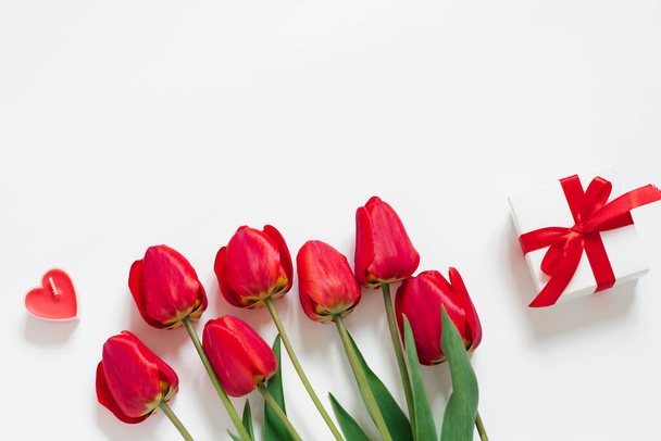 Walentynki Romantyczne tło. Czerwone tulipany, prezent z kokardą i serca świec na białym tle z przestrzenią kopiującą. Układy płaskie - Zdjęcie, obraz