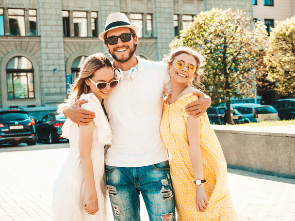 Group of young three stylish friends posing in the street. Fashion man and two cute female dressed in casual summer clothes. Smiling models having fun in sunglasses.Cheerful women and guy going crazy - Foto, afbeelding
