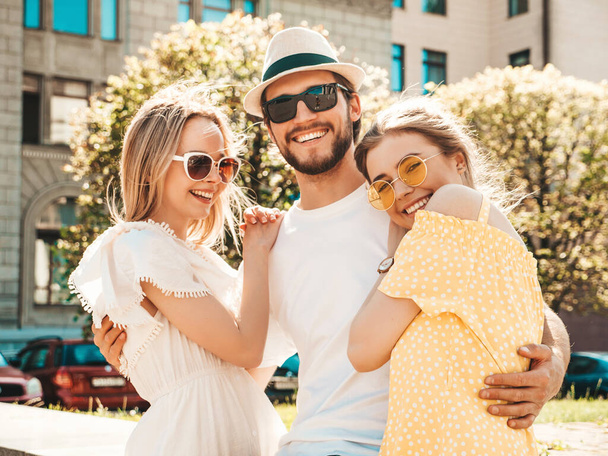 Group of young three stylish friends posing in the street. Fashion man and two cute female dressed in casual summer clothes. Smiling models having fun in sunglasses.Cheerful women and guy going crazy - Foto, Imagem
