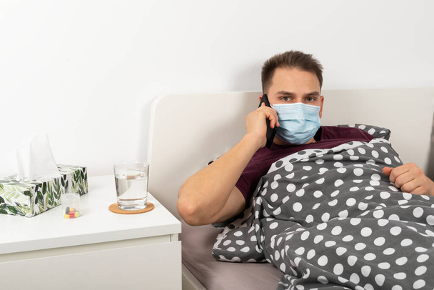Caucasian man infected with covid-19 is wearing surgical mask at home, having a call - Φωτογραφία, εικόνα