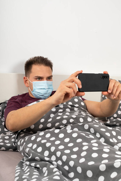 Caucasian man infected with coronavirus is wearing mask and having a video call from home quarantine - Fotó, kép