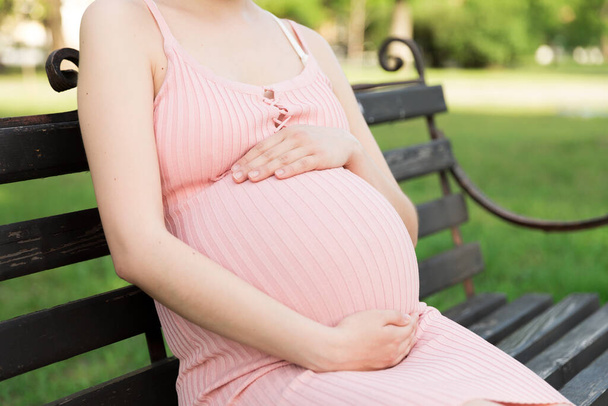 Pregnant young woman on bench sitting in the park. Pregnancy and motherhood. Healthy lifestyle. - Photo, Image