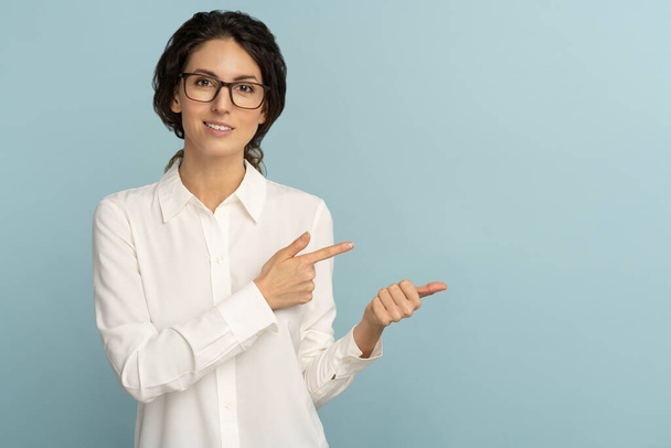 Sebevědomá podnikatelka nosí bílou blůzu a brýle ukazující prsty, ukazující na kopírovací prostor - Fotografie, Obrázek