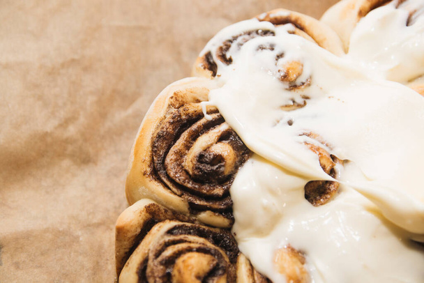 freshly baked cinnabons with cinnamon and buttercream on parchment paper. - Φωτογραφία, εικόνα