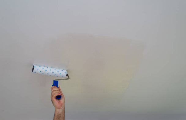 Mano sosteniendo un rodillo y pintando un techo en blanco - Foto, imagen