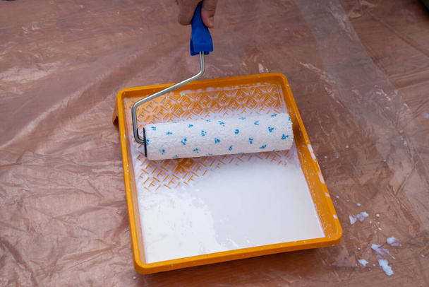 Festéktálca fehér festékkel és festőhenger a padlón védőfóliával borítva - Fotó, kép