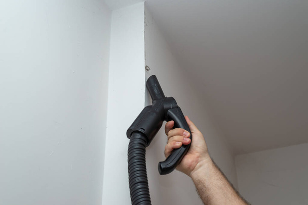 Hand of a man holding a vacuum cleaner while vacuuming dirt on a wall - Photo, Image