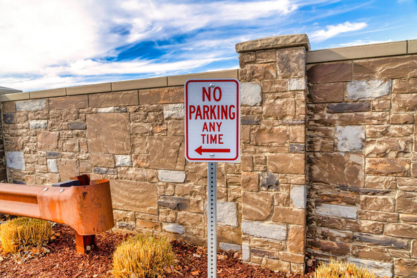 Знак "Стоянка запрещена" по соседству с каменным забором и голубым небом - Фото, изображение