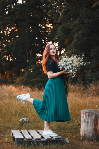 Foto di una ragazza felice con un grande mazzo di margherite bianche selvatiche in piena crescita. La ragazza in gonna turchese e scarpe da ginnastica bianche. Sorridi. Ragazza in natura - Foto, immagini