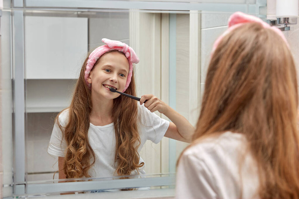 Blonde teen girl brushing her teeth in the morning in a headband. - 写真・画像