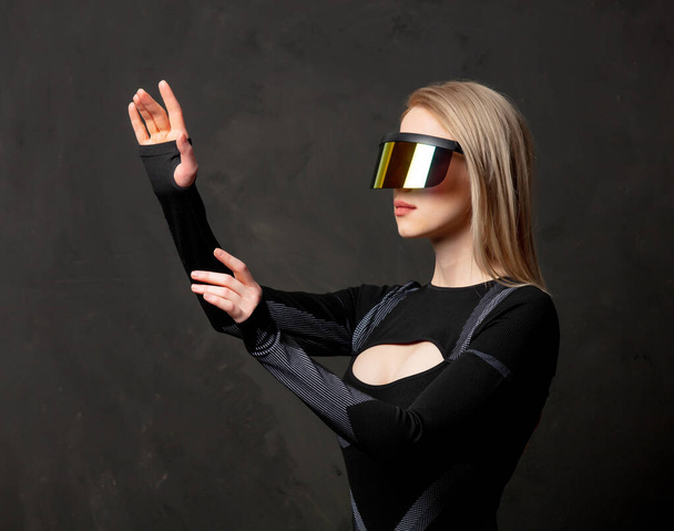 Blonde android female in VR glasses and suit on dark background. - Photo, Image
