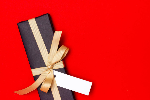 Black gift with a beige ribbon on a red background. View from above. - Fotoğraf, Görsel