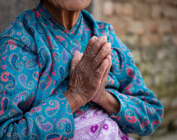 Onherkende oudere vrouw draagt blauwe doeken die haar gerimpelde handen kruisen. Verouderingsproces - Foto, afbeelding