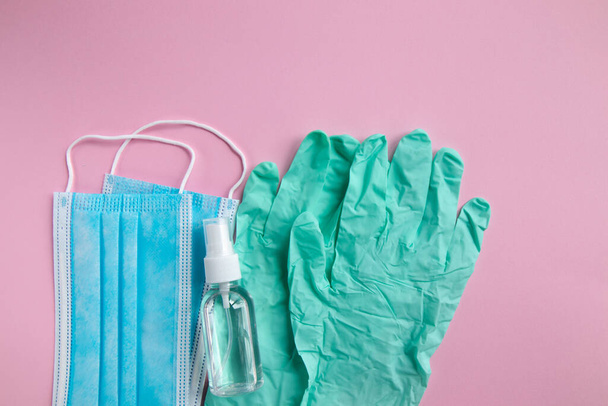 Masque médicinal, gants de protection et gel antibactérien sur fond rose. Pandémie de coronavirus. - Photo, image