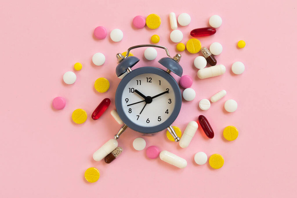 Many different pills with alarm clock on a pink background. Time to take the medicine. top view - Foto, immagini