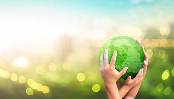 Концепция Всемирного дня окружающей среды: Семейные руки держат землю глобальной травы на размытом зеленом фоне города - Фото, изображение