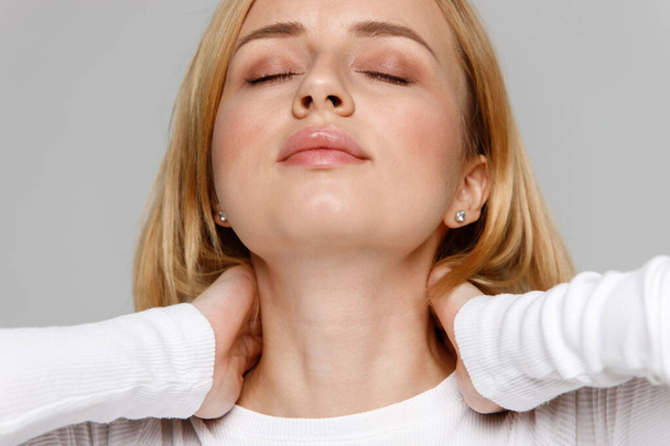 Close-up portret van jonge vrouw in witte top aanraken van haar pijn in haar nek en rug, voelt pijn, masseert het pijnlijke gebied. Baarmoederhalsartritis, osteochondrose, aandoeningen van het bewegingsapparaat - Foto, afbeelding