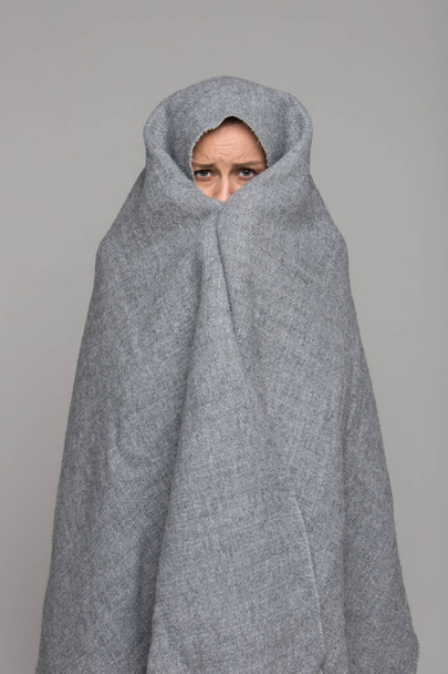 Mujer joven congelada envuelta en una bufanda cálida, cubierta con cuadros grises, es muy fría, aislada sobre fondo gris.   - Foto, Imagen