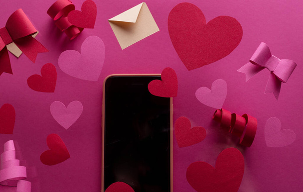 Happy st. Ystävänpäivä konsepti puhelimen ja paljon koriste punainen paperi sydämet, konfetti, jouset vastaan vaaleanpunainen tausta tilaa tekstiä. - Valokuva, kuva