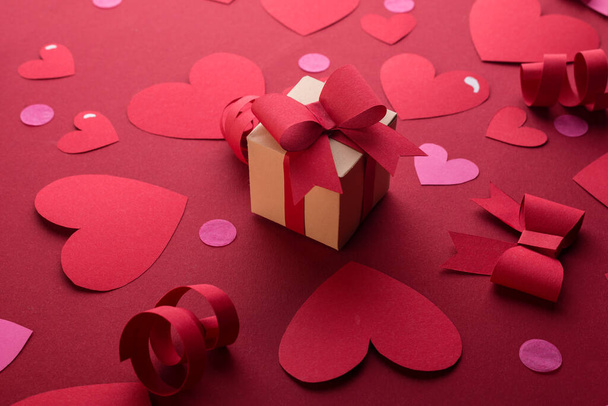 Feliz día de San Valentín concepto con caja de regalo de papel artesanal, corazones de papel rojo, arcos contra fondo rojo oscuro con espacio para el texto. - Foto, imagen