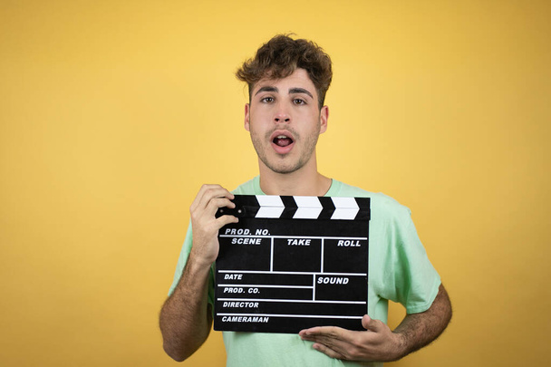 Handsome man wearing a green casual t-shirt over yellow background holding clapperboard very happy having fun - Photo, Image