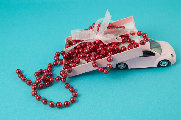 Pink retro car with a gift box on the roof with beads on a blue background. - Photo, Image