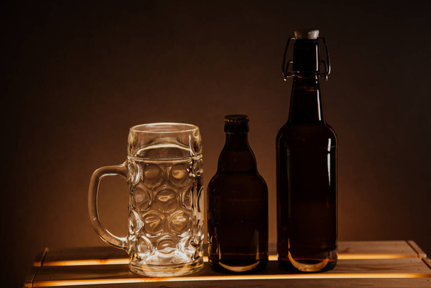 pusta butelka piwa na drewnianym stole i szklanka piwa na czarnym tle - Zdjęcie, obraz