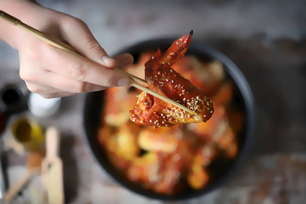 Selectieve focus. Mannelijke hand met eetstokjes houdt pittige kippenvleugels. Kippenvleugels in Chinese stijl. - Foto, afbeelding